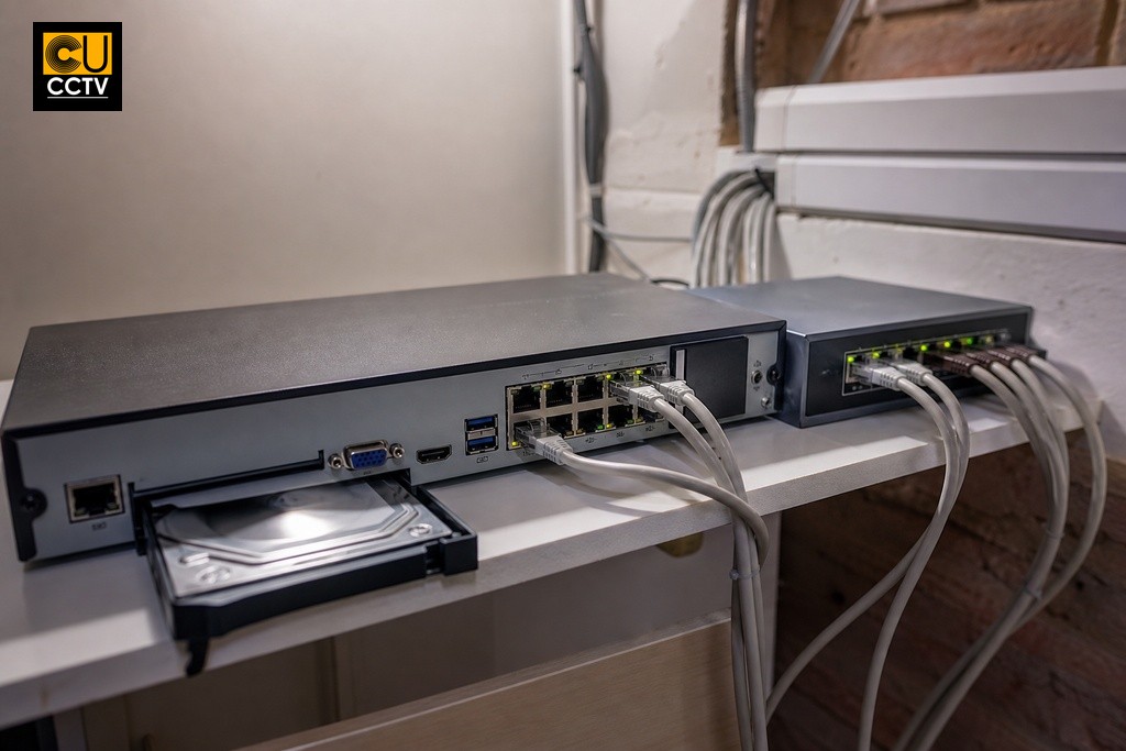 PoE switch with Ethernet cables connected to NVR recorder in a small UK property network cabinet